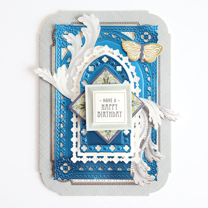 A decorative handmade birthday card with layered blue, white, and silver designs, ornate cutouts, a gold butterfly, and a central message reading "Have a Happy Birthday.