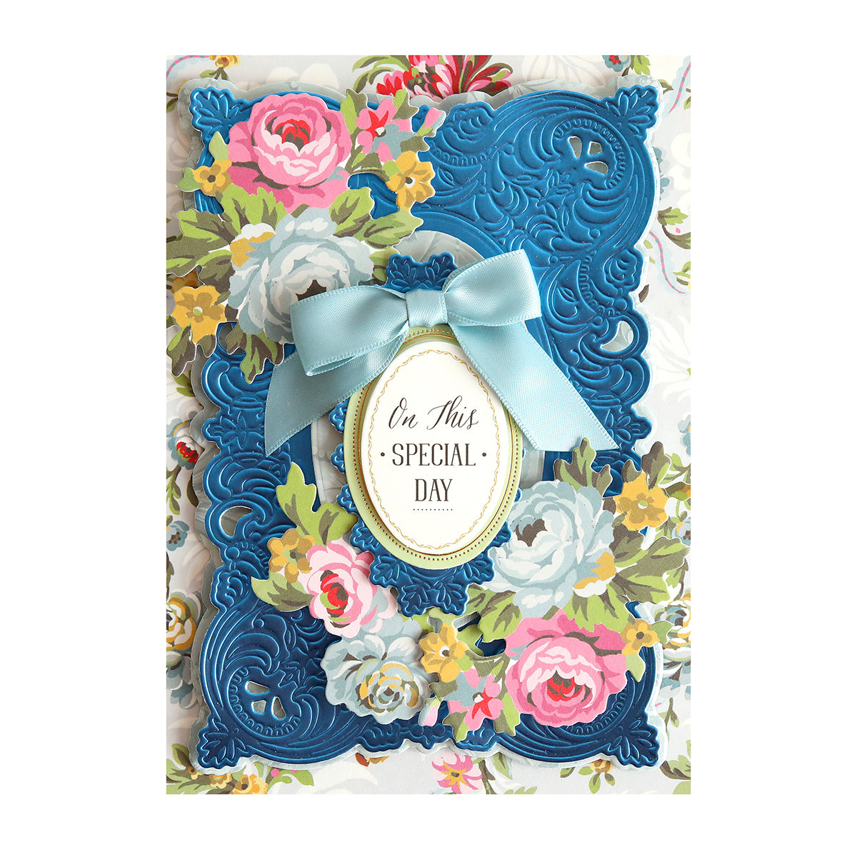 A floral greeting card with embossed blue frame, light blue bow, and an oval label that reads "On This Special Day.