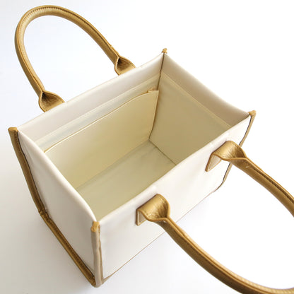 An open, empty ivory and gold palette Empress Mini Machine tote bag with gold-colored handles and trim against a white background.