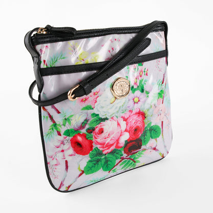 The Lillian Crossbody is a shoulder bag featuring a floral pattern, crafted from laminated cotton with a black strap and gold button detail, displayed against a white background.