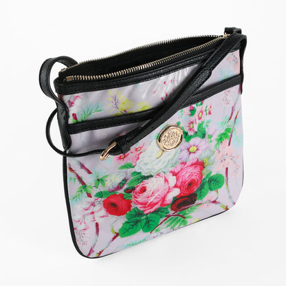 The Lillian Crossbody, crafted from laminated cotton with a floral pattern, features black trim, a gold medallion detail, and a zippered top—shown against a white background.