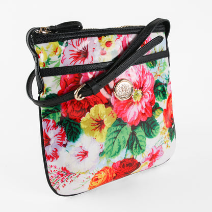 The Annalise Crossbody Bag is a small rectangular floral shoulder bag featuring black trim and strap, accented with a gold circular embellishment on the front, shown against a white background. This stylish laminated cotton purse offers women the perfect combination of durability and charm.