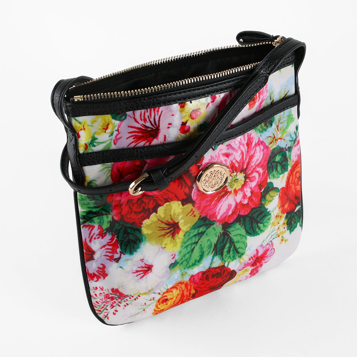 Introducing the Annalise Crossbody Bag: a women’s shoulder bag crafted from laminated cotton with a floral pattern, styled with black trim, a gold zipper, and finished with a round gold emblem on the front.