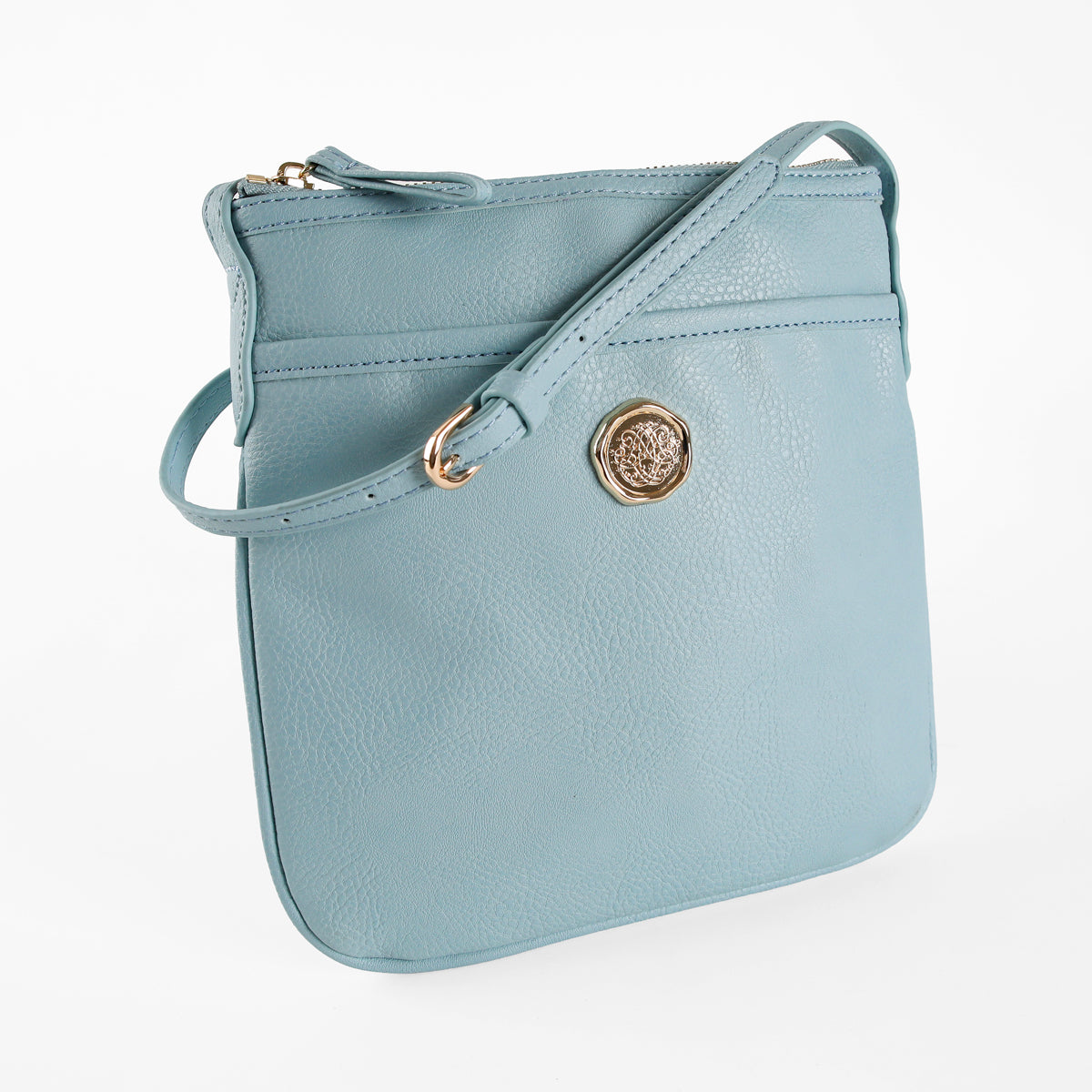 The Beach Glass Blue Crossbody Bag, crafted from light blue faux leather with a gold emblem and zipper closure, features an adjustable strap for comfortable crossbody wear and is pictured against a white background.
