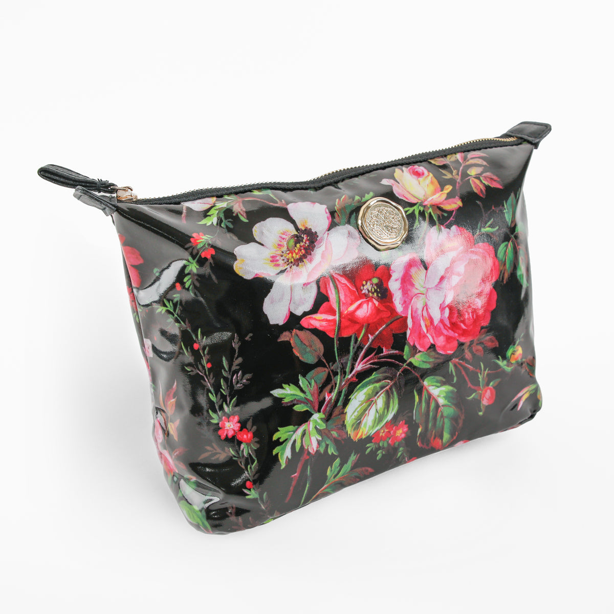 The Noire Large Cosmetic Bag is a glossy black zippered pouch adorned with a floral pattern of pink and white flowers and green leaves, accented by a round metal emblem on the front. Ideal as a spacious cosmetic bag or travel organizer, it keeps your essentials stylishly organized wherever you go.