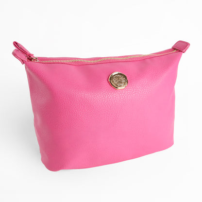 The Raspberry Pink Large Cosmetic Bag is a faux leather zippered pouch featuring a gold circular emblem on the front, displayed against a white background. This spacious makeup bag also functions as a stylish travel toiletry bag, offering both elegance and practicality for your essentials.