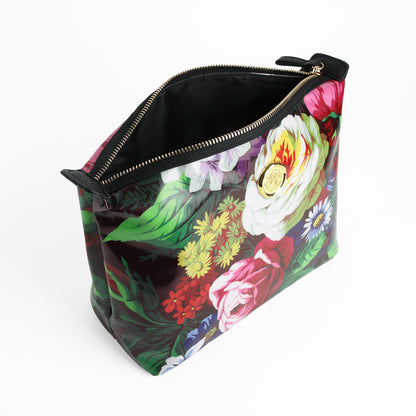 The Astrid Large Cosmetic Bag, crafted from laminated cotton with a chic floral design, features a zippered closure adorned with a gold emblem and opens to reveal its sleek black interior, all displayed against a crisp white background.