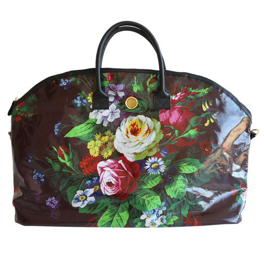 A floral-patterned, dome-shaped Astrid Duffle Bag with vibrant multicolored flowers and green leaves on a translucent brown background, featuring black handles and a gold clasp.