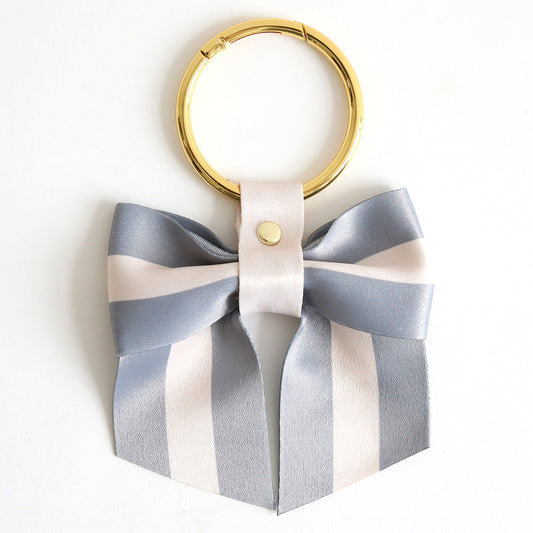 The Gray Stripe Bag Charm features a stylish keyring with a decorative gray and white striped ribbon bow, making it a chic accessory for your bag.