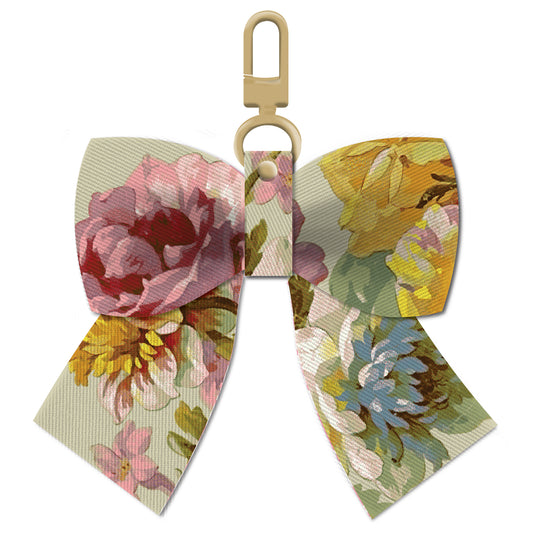 The Francesca Bag Charm features a floral fabric bow adorned with pink, yellow, and blue flowers on a light background. With its gold clasp, this twill bow makes the perfect accessory for your bag.