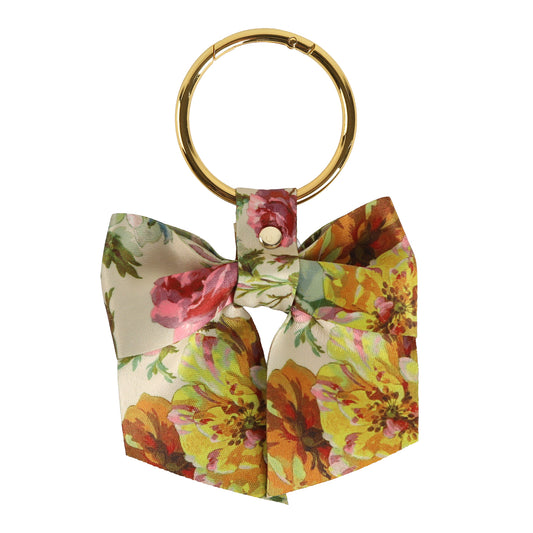 The Francesca Bag Charm is a gold keyring adorned with a fabric bow in a vibrant floral print of yellow, green, red, and pink—an enchanting accessory that adds the perfect decorative touch to your purse.