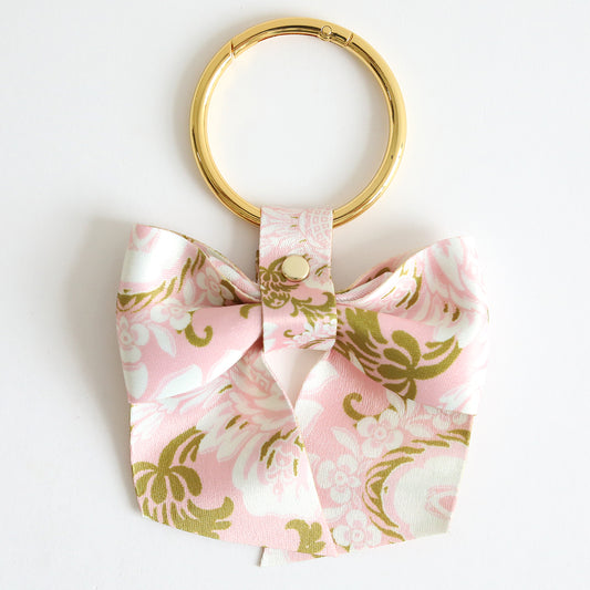 The Pink Damask Bag Charm features a gold keyring with a pink and gold floral twill bow—ideal as a charming accessory for your bag.