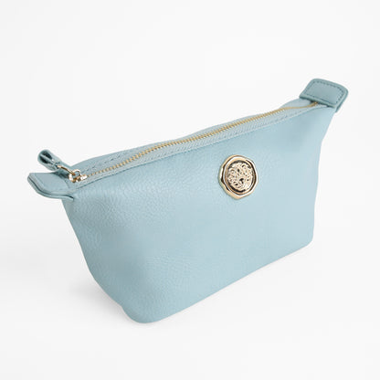 The Beach Glass Blue Small Cosmetic Bag features light blue faux leather and a gold circular emblem on the front, shown against a plain white background—perfect for use as a travel cosmetic pouch or small makeup bag.