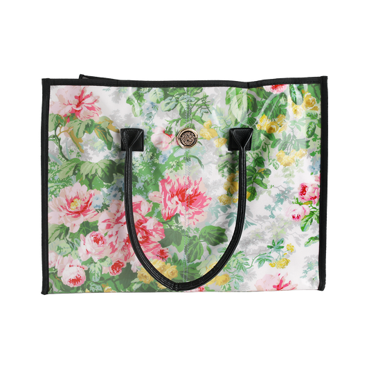 The Virginia Tote Bag is a spacious, laminated cotton tote with black handles and trim, showcasing a vibrant floral pattern on a white background.