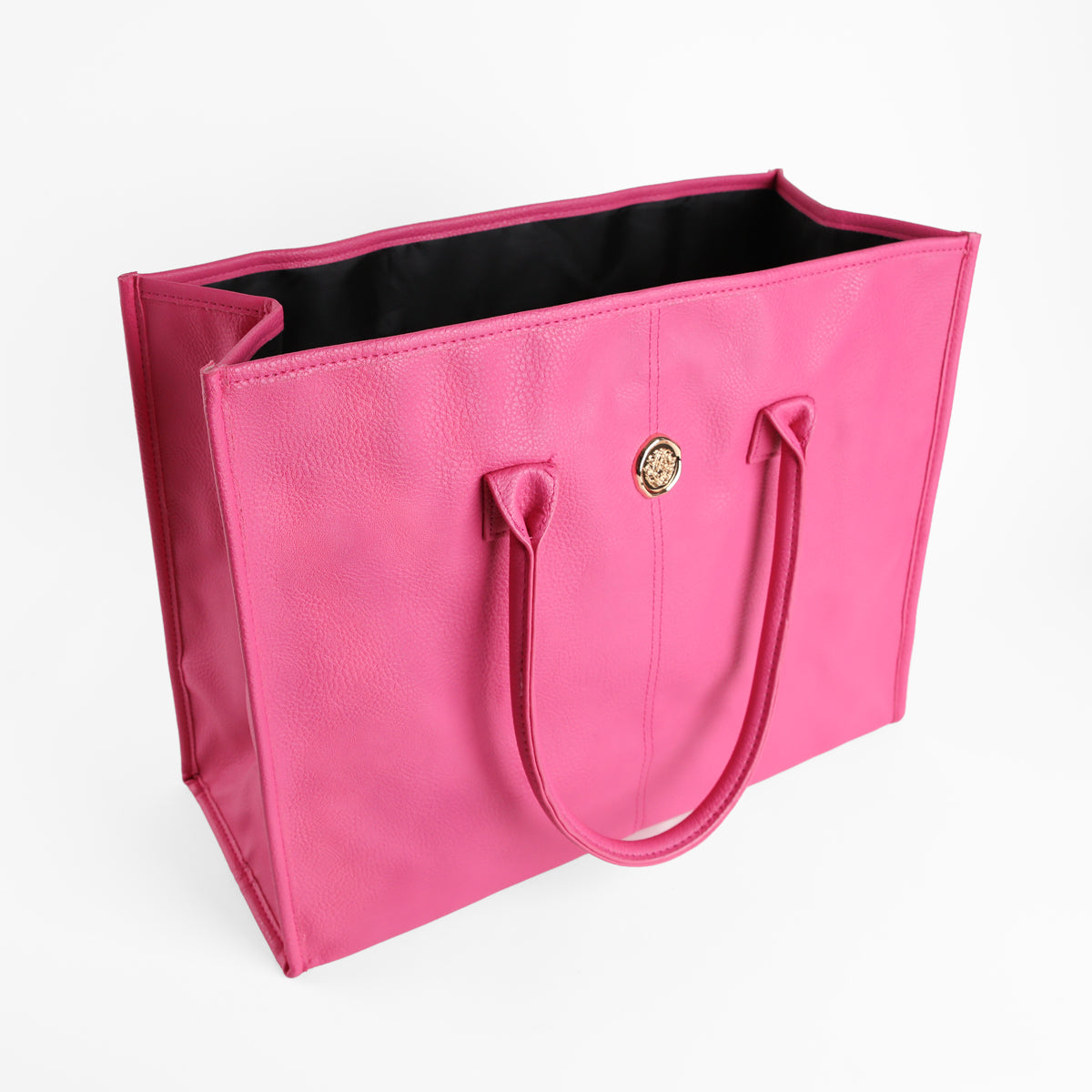 The Raspberry Pink Tote Bag is a spacious tote crafted from premium faux leather in a vibrant pink hue, featuring two sturdy handles, a gold-colored circular emblem on the front, and a sleek black interior—all showcased against a white background.