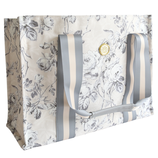 The Faded Rose Tote Bag features a durable gray and white floral print, wide striped handles, and a gold emblem on the front—perfect for everyday use.