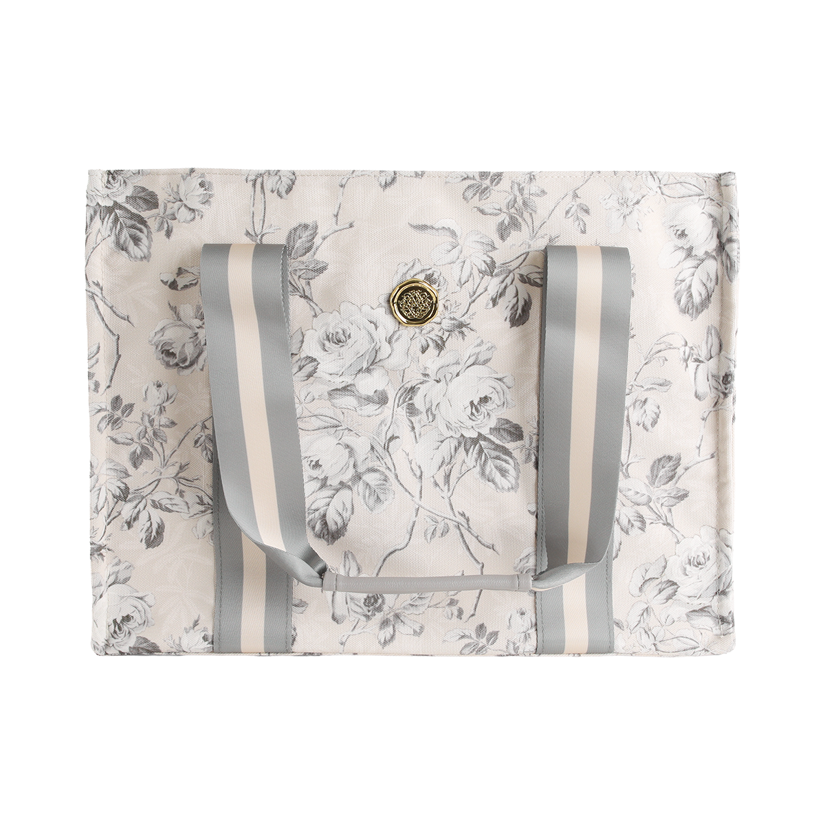 The Faded Rose Tote Bag features a rectangular canvas design with a gray and white floral print, double gray striped handles, and a round gold emblem on the front—making it the perfect stylish floral market bag.