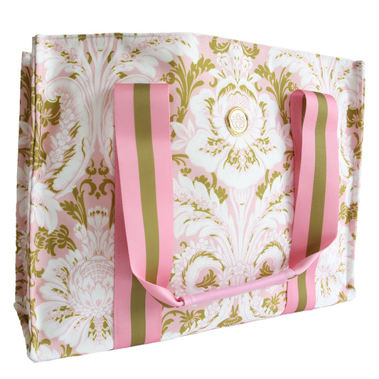 The Pink Damask Tote Bag features a pink and gold floral pattern, matching striped handles, a round gold emblem on the front, and is made from durable cotton—perfect for everyday use.