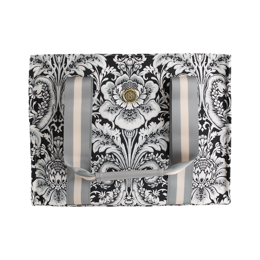 The Damask Noire Tote Bag features an ornate black and white floral damask pattern on a rectangular silhouette, complemented by vertical gray and cream straps and a central gold decorative button.