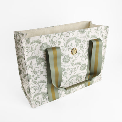 Green Climbing Rose Tote Bag featuring a rectangular shape, green climbing rose floral pattern, wide green striped handles, and a gold circular emblem on the front, displayed on a white background. This stylish canvas market bag makes an ideal botanical gift for women.