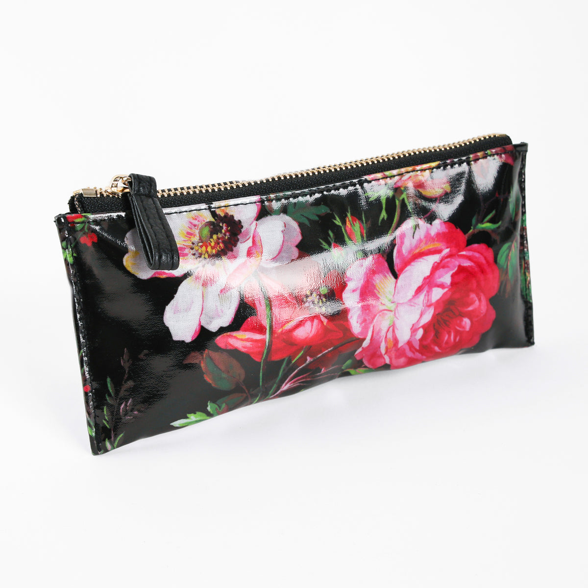 Introducing the Noire Pencil Case—a rectangular, black zippered pouch crafted from glossy laminated cotton and adorned with a floral print featuring pink and white flowers. Perfect as a stylish zippered pencil case or a chic desk accessory gift.