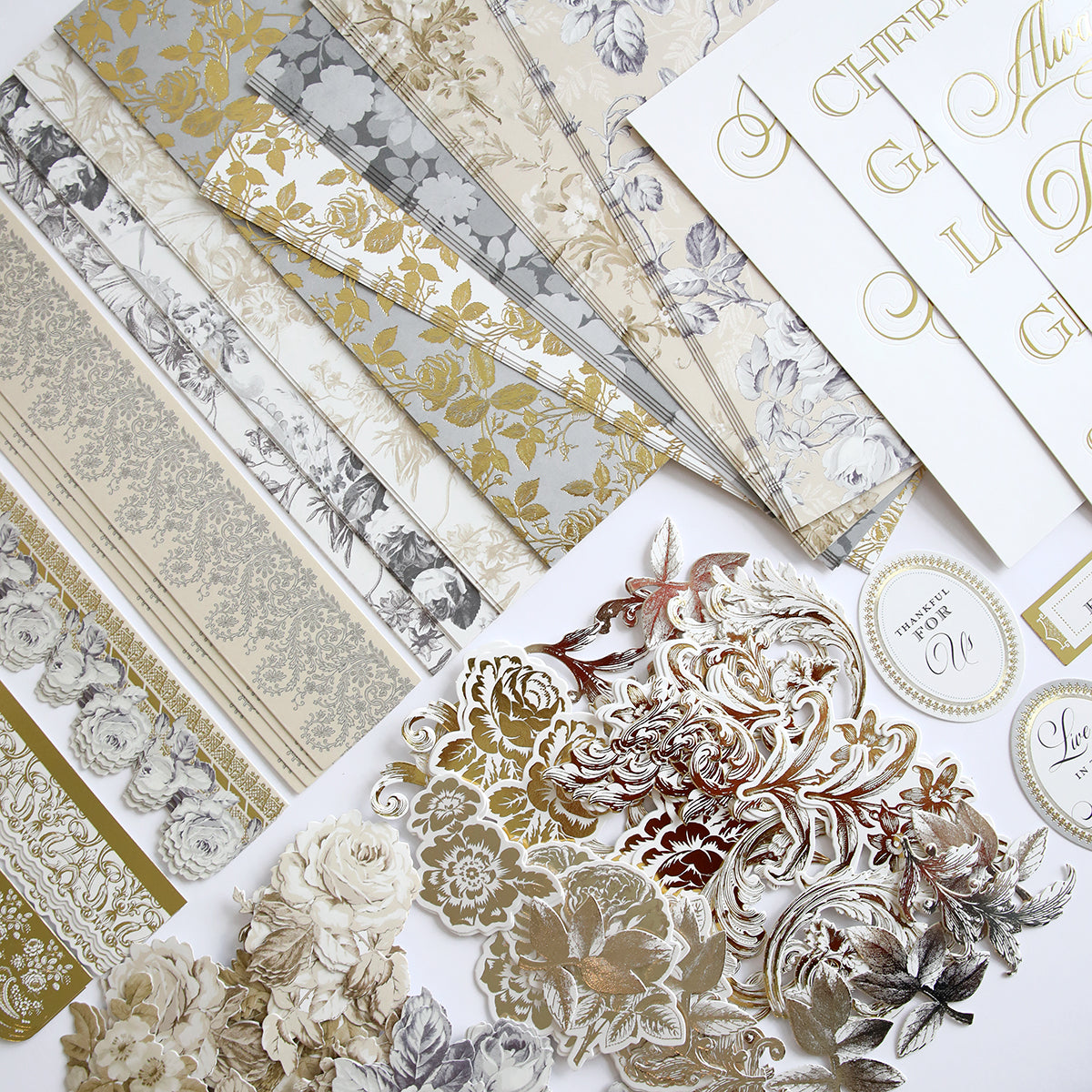 An assortment of elegant, gold and silver floral-patterned papers and cardstock, with various intricate designs and calligraphy elements, laid out on a white surface, featuring **Faded Rose Papers and Embellishments** to add a touch of vintage charm.