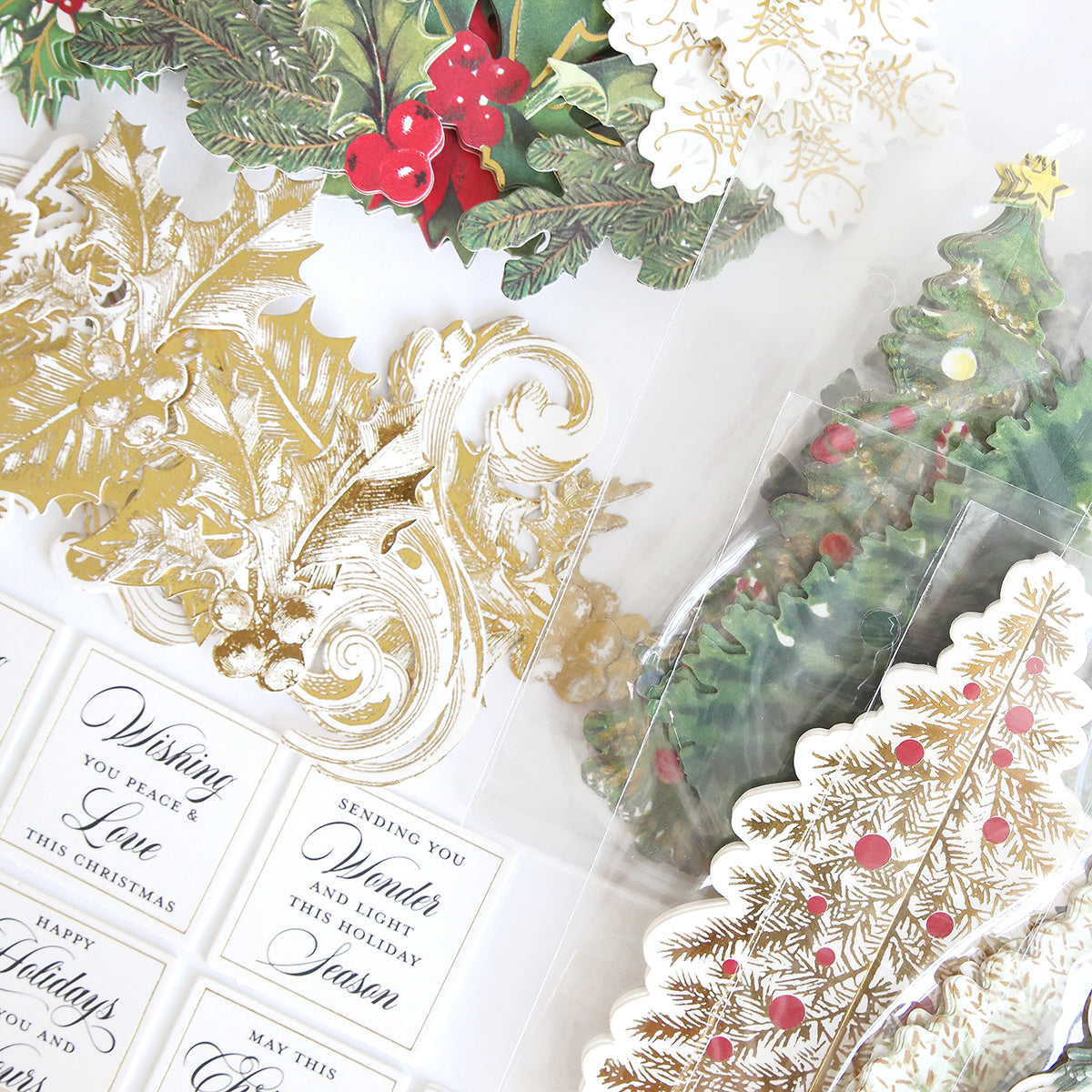Assorted Christmas-themed stickers featuring gold holly, pine branches with red berries, decorated Christmas trees, and holiday greeting labels arranged on a white surface—perfect embellishments for your handmade cards or to complete the Folded Christmas Tree Card Making Kit.