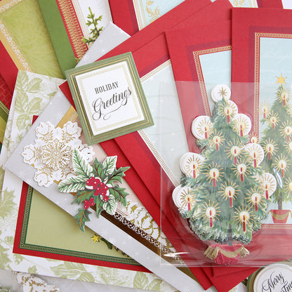 A set of handmade Christmas cards and decorations created with the Folded Christmas Tree Card Making Kit, featuring a “Holiday Greetings” card, holly, snowflakes, and a folded Christmas tree card, all displayed on a flat surface.