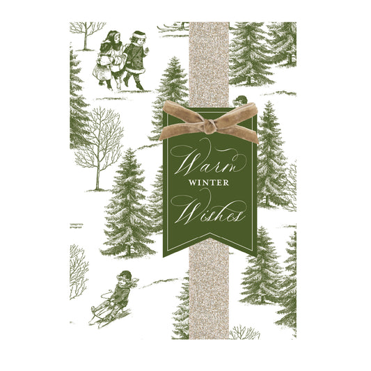 The Winter Toile Boxed Card 10 ct features handmade holiday cards with vintage-style illustrations of children playing in the snow, a gold glittery vertical ribbon, and a green tag that says “Warm Winter Wishes.”.