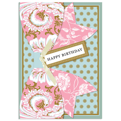 The Pink Damask Birthday Bow Card features a decorative pattern in pink, white, and gold foil with a large bow and "Happy Birthday" message on a blue background sprinkled with gold dots. It includes warmest wishes for your special day.