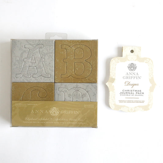 The Holiday Chipboard Letters and Journaling Tags include a collection of ornate alphabet cards with letters 'A', 'B', and 'C' in gold and silver tones, perfect for enhancing scrapbook pages. This set pairs beautifully with a Christmas journal pack, all elegantly encapsulated in decorative white and gold packaging.