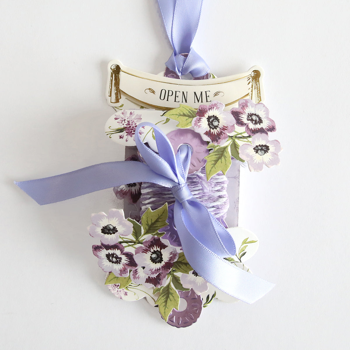 A custom Gift Tag Compendium Class Materials and Dies, handmade with care, hangs from a purple ribbon by Anna Griffin.