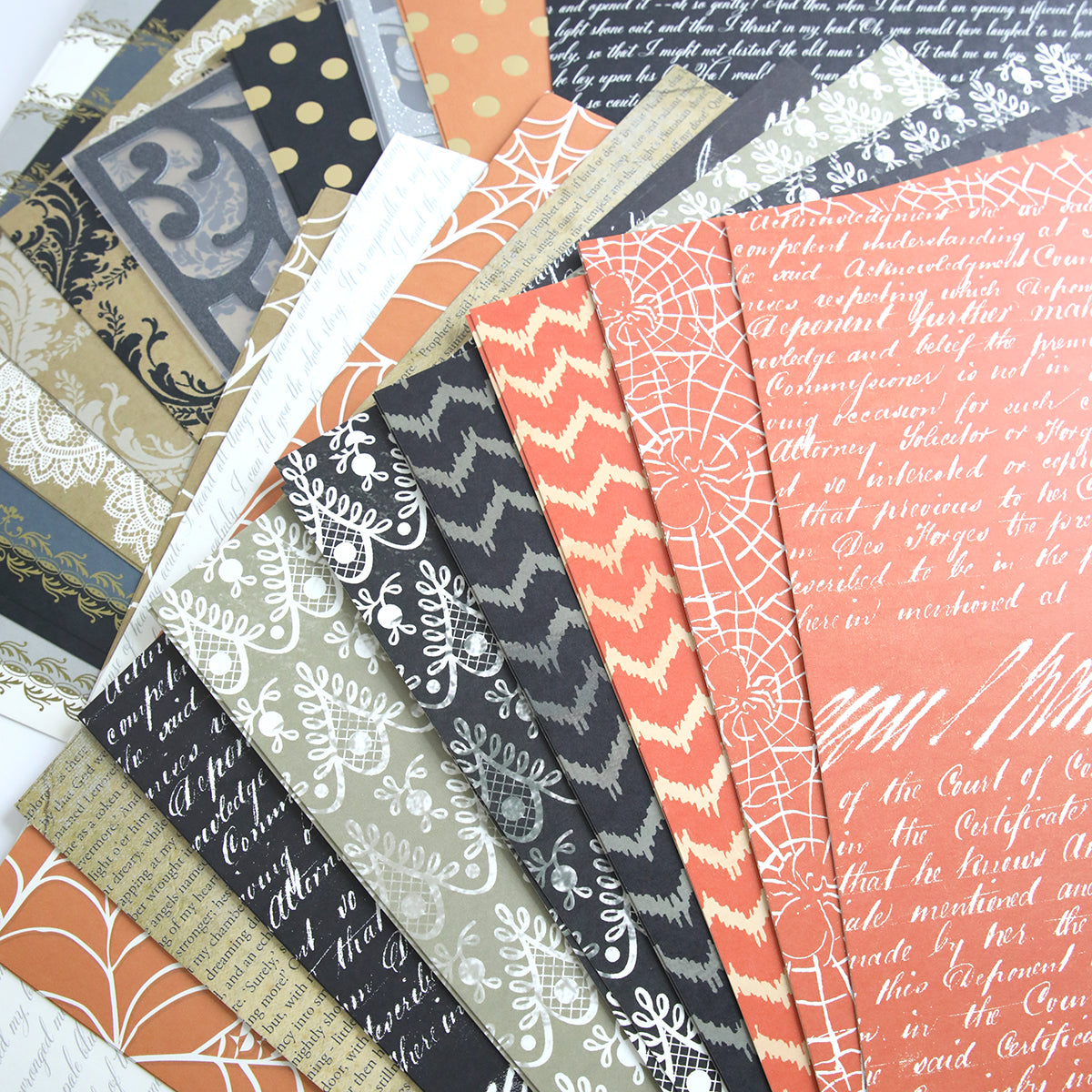 A fan arrangement of various scrapbook papers from the Haunted Halloween 12x12 Cardstock collection, featuring multiple patterns and colors including black, orange, and beige with designs such as text, lace, zigzag, webs, and leaves.