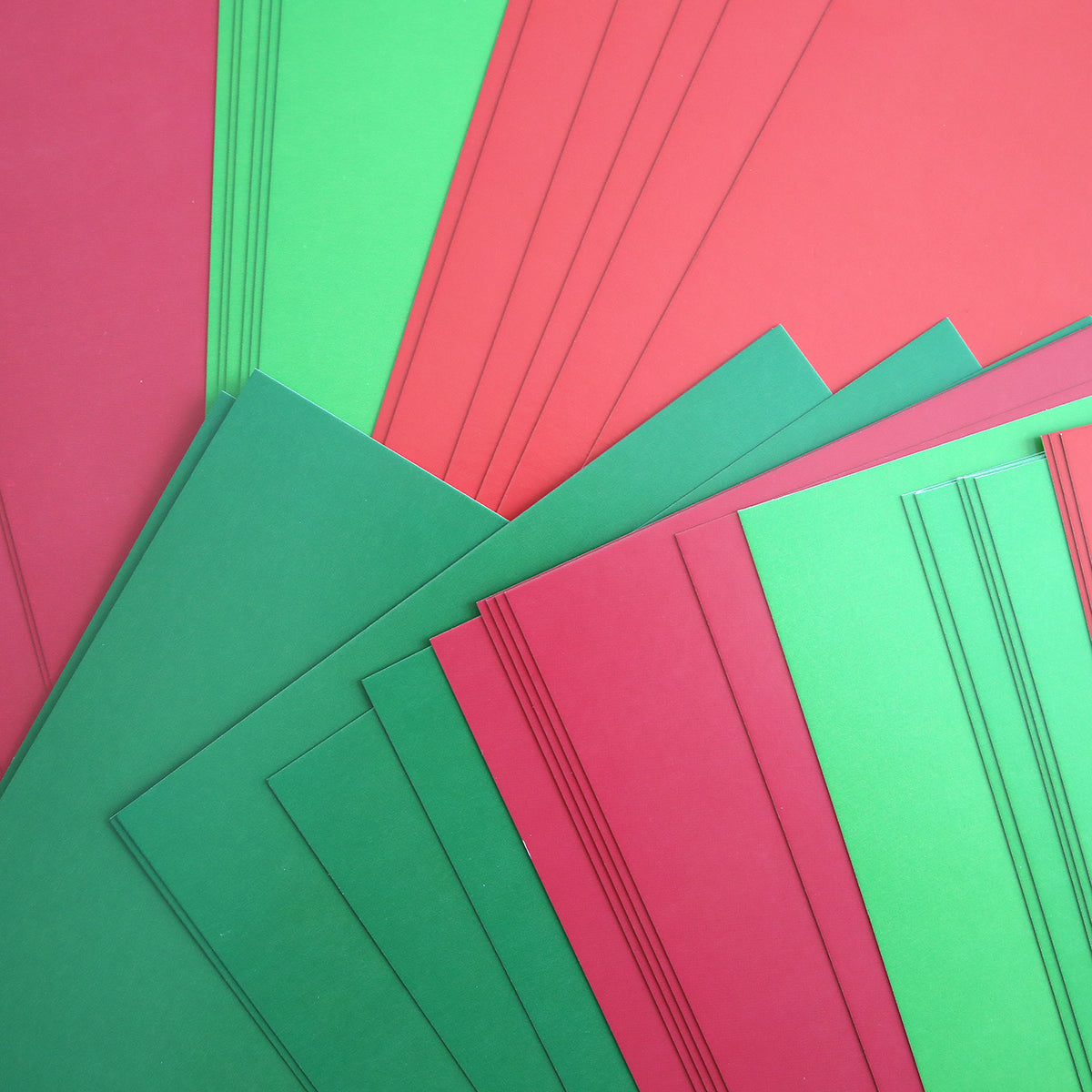 Holiday Coated Cardstock sheets in red and green are arranged in a fan pattern, overlapping each other on a flat surface.