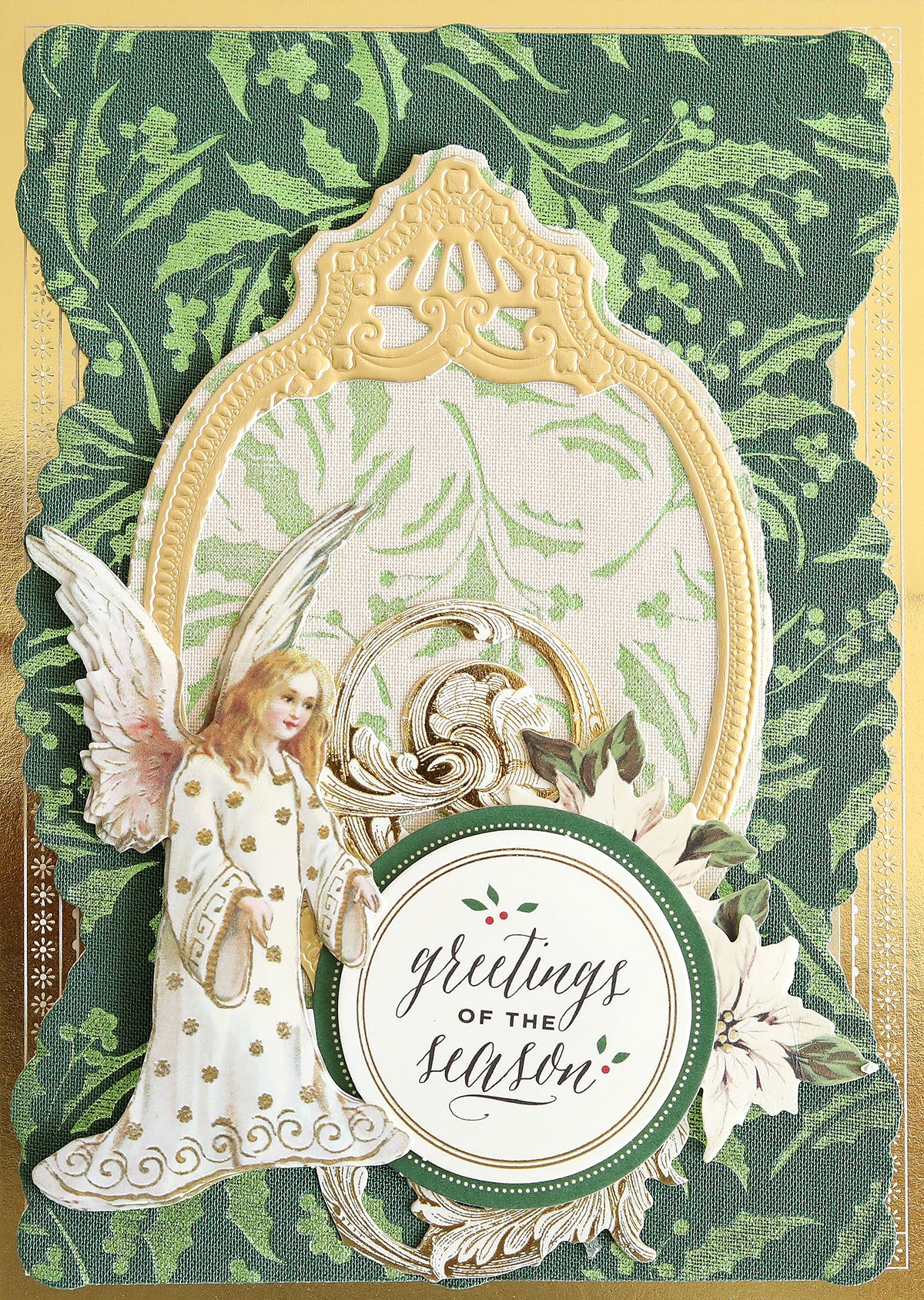 Featuring Holiday Fabric Card Layers, this holiday card showcases an angel illustration framed in ornate gold, a circular “greetings of the season” label encircled by poinsettia flowers, and a green patterned background. Perfect for Christmas card making, these fabric layers add rich texture and elegance to your design.