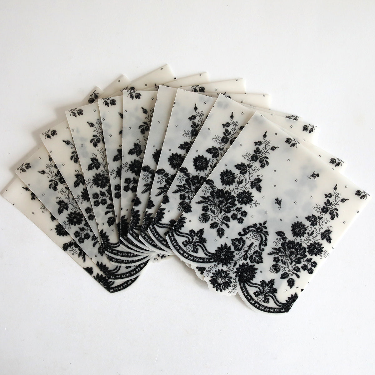 The Black Lace Petticoat Vellum Wrap 10 pack features ten translucent sheets with black floral patterns, beautifully fanned out on a white background.
