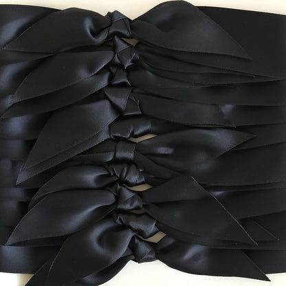 A close-up of several Black Satin Knots (10 count), perfect for handmade cards, arranged neatly in an overlapping row.