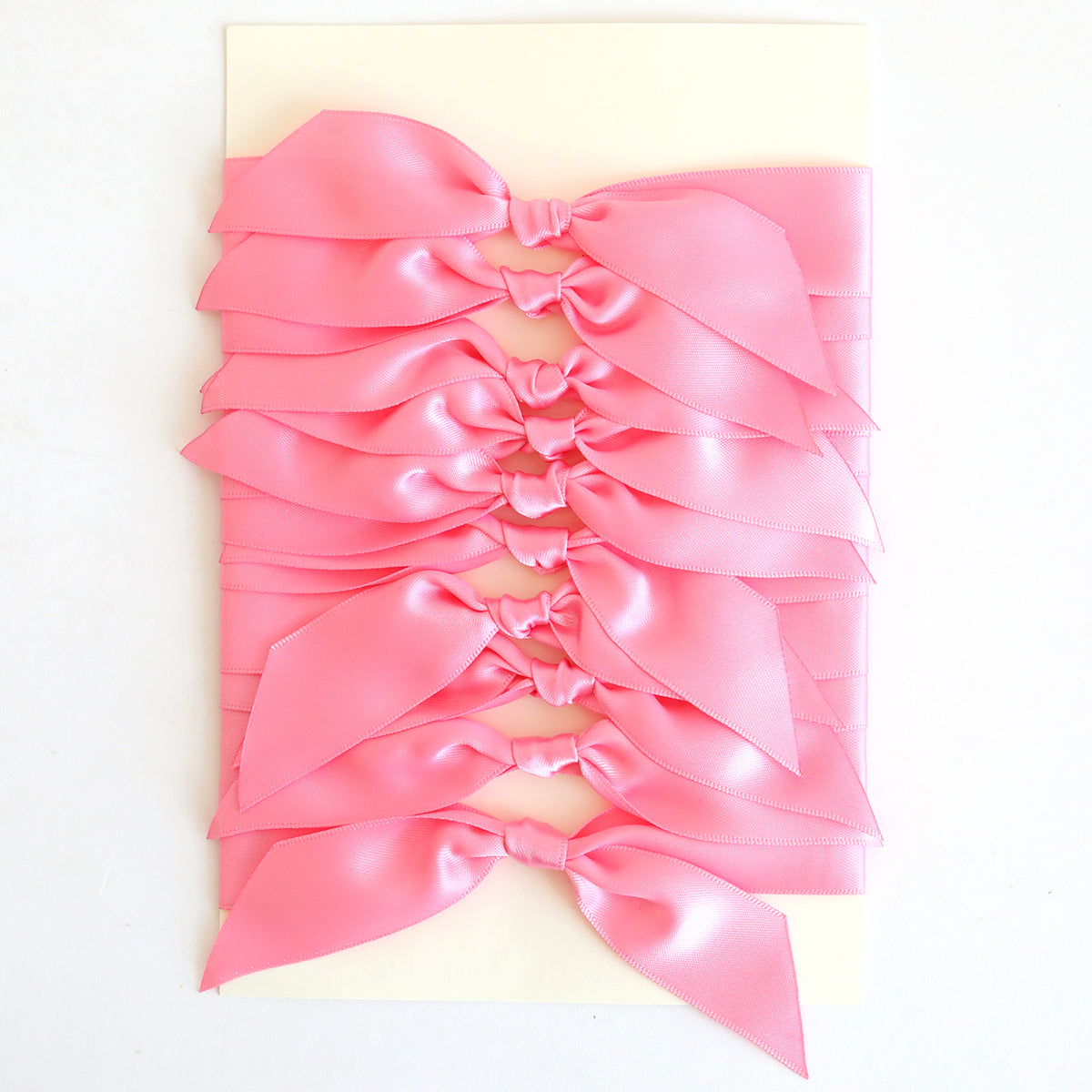 Ten pink satin knots are neatly arranged on a rectangular white card, perfect for embellishing your handmade cards.