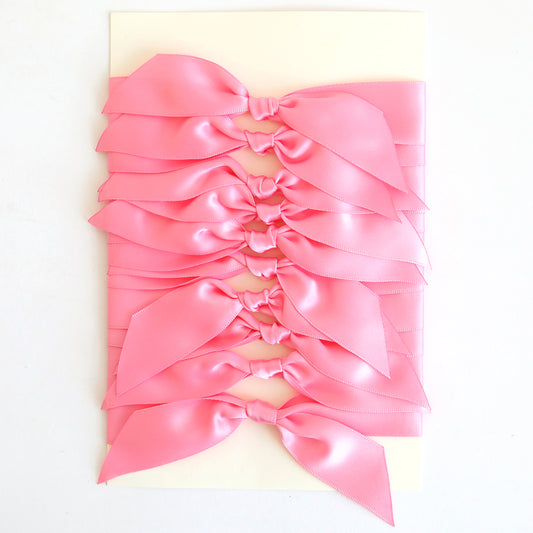 Ten pink satin knots are neatly arranged on a rectangular white card, perfect for embellishing your handmade cards.