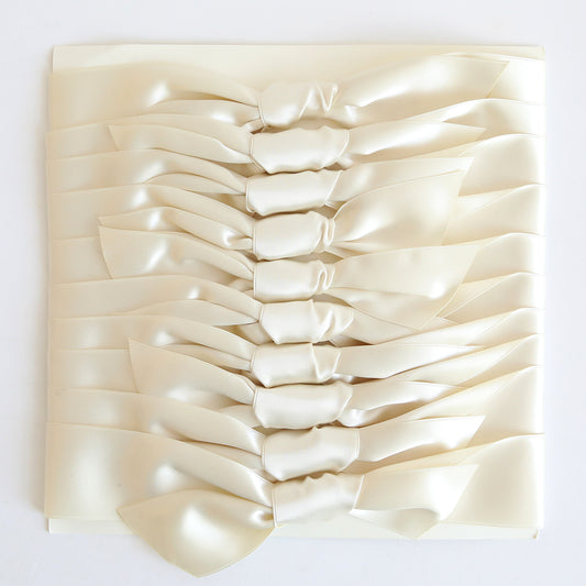 A stack of ten ivory satin knots, styled like bow ties, neatly arranged on a white surface.