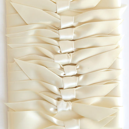 A close-up of Ivory Satin Knots 10 count—cream-colored, double-faced satin bows neatly arranged in overlapping rows, ideal as elegant pre-tied ribbons or embellishments for handmade cards.