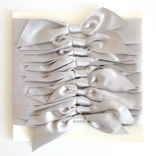 Ten elegant Silver Satin Knots are neatly arranged in parallel rows on a flat white surface, ideal for decorating handmade cards.