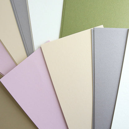 The Luxury Shimmer Cardstock - Antique, featuring a range of pastel hues such as beige, pink, green, and gray, is elegantly displayed fanned out on a flat surface.