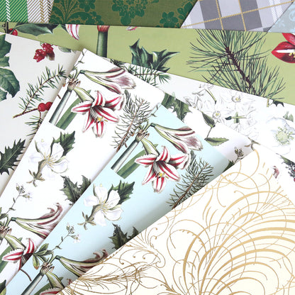 Mystery Christmas 12x12 Cardstock sheets, featuring festive botanical and geometric designs like holly, lilies, pine branches, and gold swirls, are arranged in a fan shape—perfect for your holiday crafts.