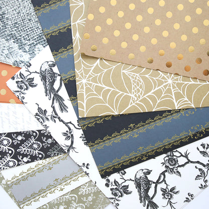 The Mystery Halloween 12x12 Cardstock set includes fan-arranged sheets with patterns like polka dots, spider webs for Halloween, birds on branches, lace, and decorative borders.