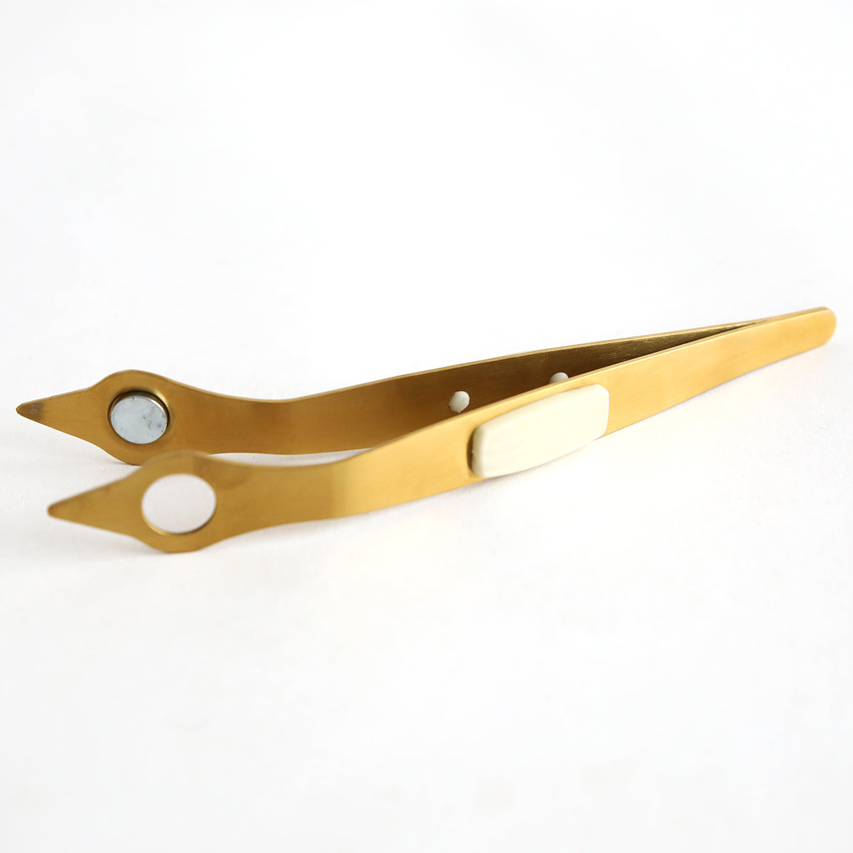 A pair of gold Magnetic Tweezers on a white surface.