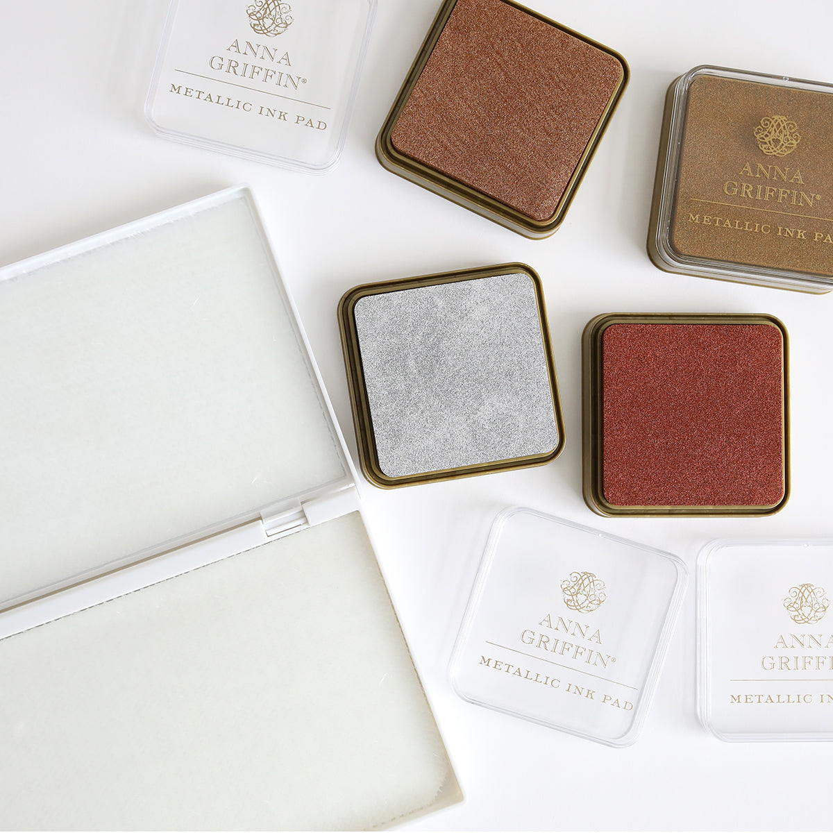 Flat lay of various Metallic Ink Pads in gold, silver, and bronze from Anna Griffin, alongside two ink pad cases and a stamp cleaning pad.