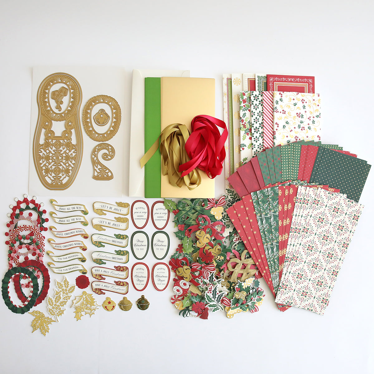 A neatly arranged assortment of crafting supplies, including patterned paper, gold cutouts, ribbon, tags, and various embellishments on a white surface. The Paper Elf Shoe Finishing School Craft Box will also feature playful additions such as Paper Elf Shoes and is scheduled for shipping at the end of July.