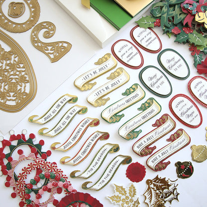 Assorted Christmas craft supplies, including decorative cutouts, cards, and festive messages like "Let's Be Jolly" and "Merry Christmas," are arranged neatly on a white surface. A whimsical touch is added by a pair of adorable Paper Elf Shoes from the Paper Elf Shoe Finishing School Craft Box.