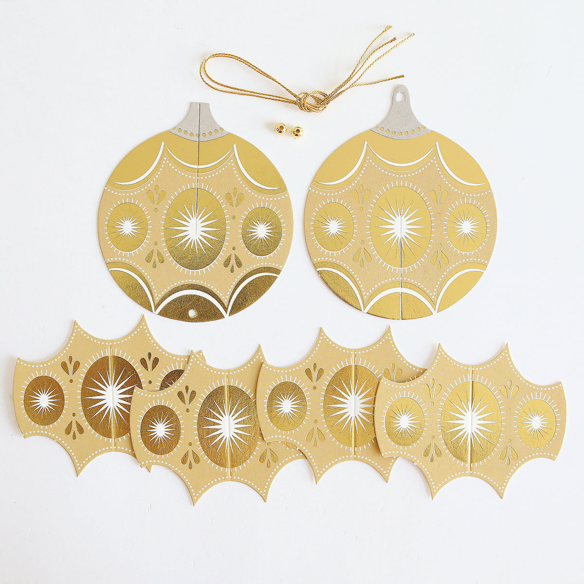 Gold and silver cardstock ornament pieces, a gold string, and two small gold beads are displayed on a white surface—ready for assembly with the Paper Ornaments Advent Calendar or as festive decor accents.